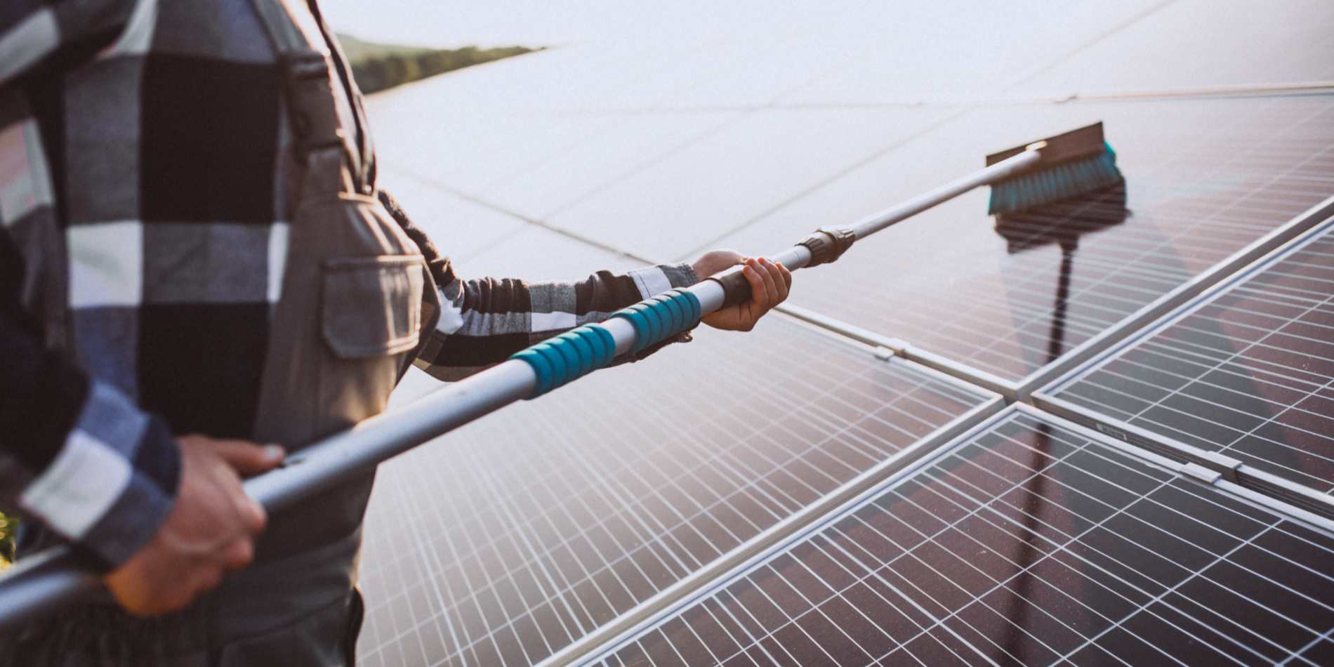 A worker cleans solar panels with a long brush, ensuring optimal sunlight absorption on a sunny day.