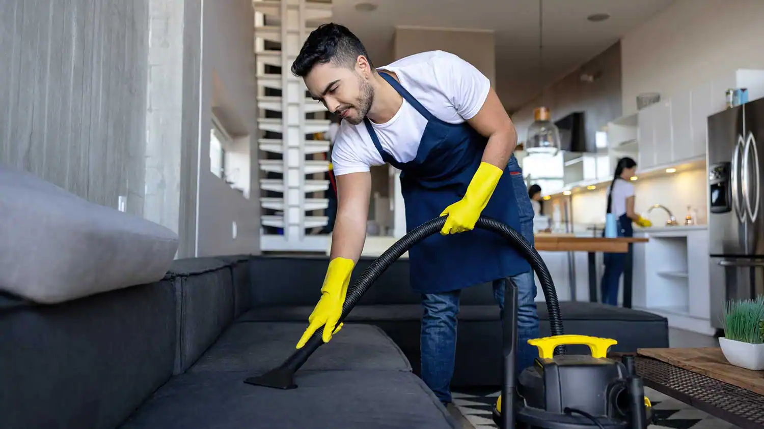 Man cleaning a sofa at home using a vacuum cleaner and protective equipment, keeping the environment clean and organized.
